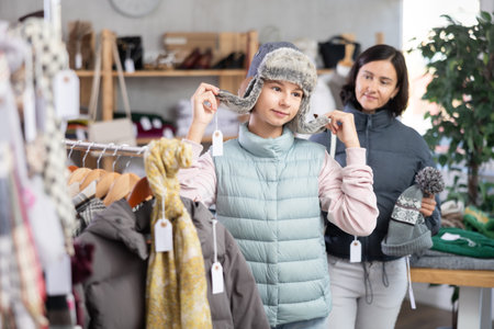 Adolescence girl try on fur hat during shopping with mother in clothes storeの写真素材