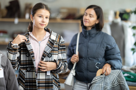 Teenage girl with her mother try on coat in storeの写真素材