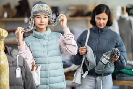Teenage girl with her mother try on fur hat in storeの写真素材