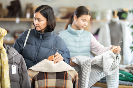 Mother and teen daughter looks at products in store and selects coat or jacket for childの写真素材