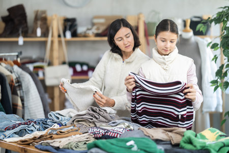 Mother and teen daughter looks at products in store and selects knitted jumper.の写真素材