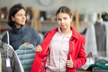 Adolescence girl try on red coat during shopping with mother in clothes storeの写真素材