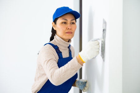 Woman builder using floated trowel to daub plaster to wallの写真素材