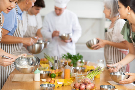 Cooking course - male chef in cook uniform teaches young people cooking class students to prepare and mix ingredients for dishes in restaurant kitchenの写真素材