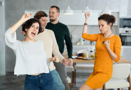 Friends dancing. Cheerful young people dancing and drinking while enjoying home party on roomの写真素材