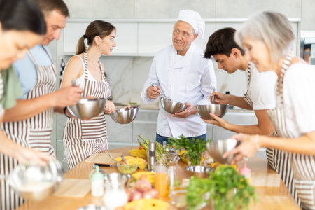 Smiling old man chef of cooking course teaching attendees how to mix sauceの写真素材
