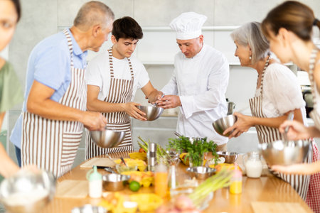 Cheerful middle-aged man chef of cooking course teaching attendees how to mix sauceの写真素材