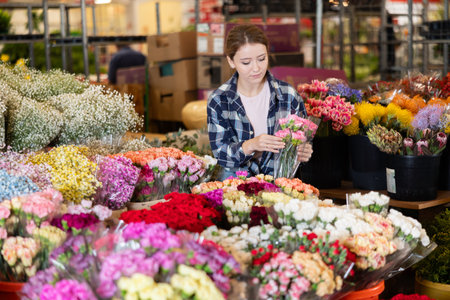 Girl flower shop assistant collects carnations into bouquetの写真素材