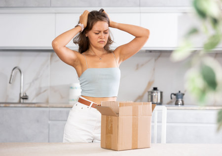 Young upset woman holding open box in kitchenの写真素材