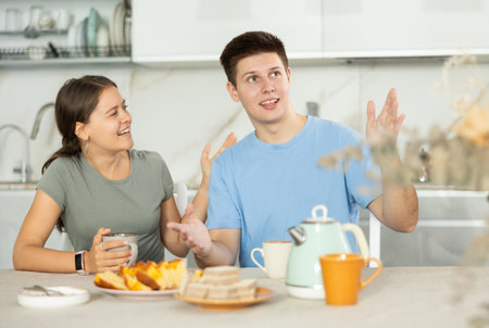 Happy young couple sitting at the kitchen-table and having conversation while drinking teaの写真素材