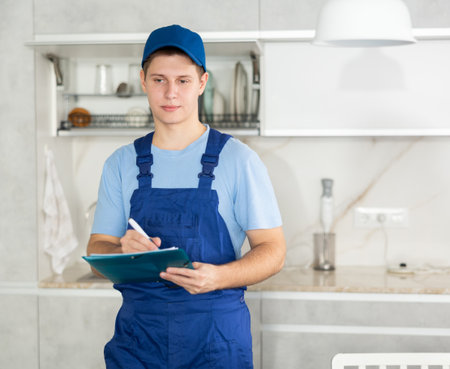 Young technician of cleaning company writing down order in residential kitchenの写真素材