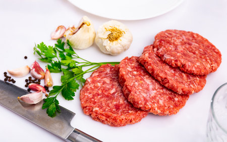 Raw beef patties for burgers with greens, garlic and allspice on tableの写真素材