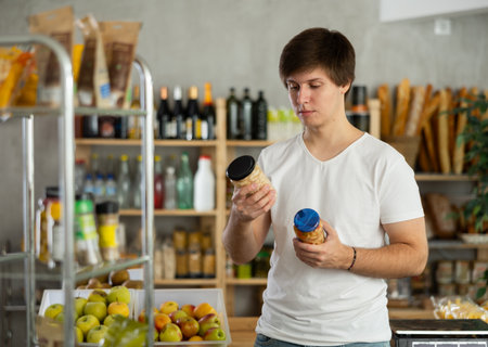 Young man carefully choosing canned beans at grocery storeの写真素材