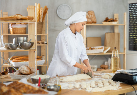 Baker girl cuts small pieces of dough from large lump and puts them on scales.