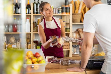 Young woman seller offers cheese and meat to buyerの写真素材