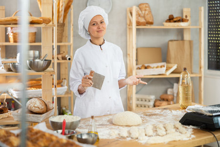Female baker in uniform cutting raw dough with knife to make croissants or buns