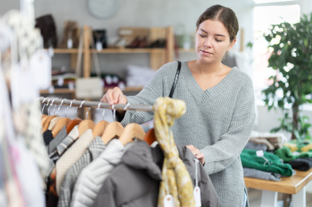 Interested happy young girl standing in clothing shop and looking something on sale of winter clothing collectionの写真素材