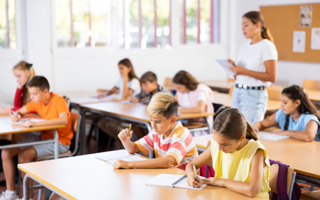 Boys an girls sitting at lesson in classroom, teacher standingの写真素材