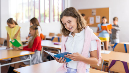 Happy tween schoolgirl sitting on table with notebook during breakの写真素材