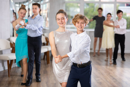 Positive teen boy and girl are dancing classic version of waltz in couple during lesson at studio