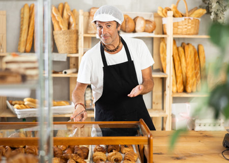 Portrait of friendly baker selling fresh baguettes and croissants in bakery
