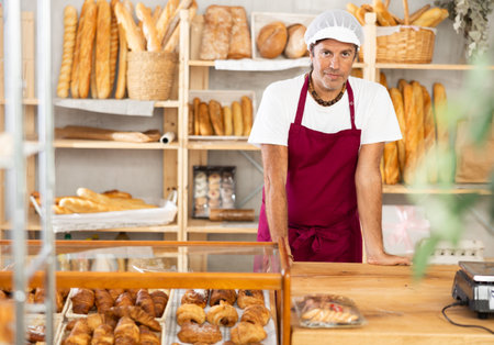 Portrait of friendly baker selling fresh baguettes and croissants in bakery