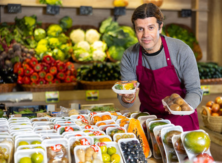 Male grocery store worker offers various packaged ripe fruits and vegetables