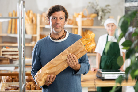 Man buyer with baguettes in package stands near showcase in bakeryの写真素材