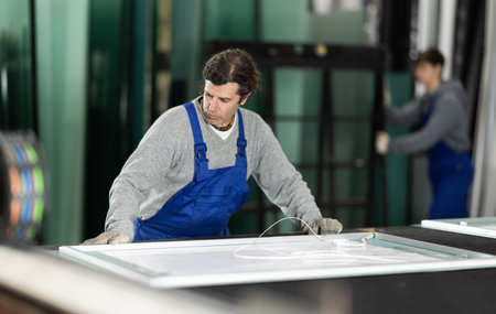 Man glazer employee in blue overall works in glass processing shopの写真素材