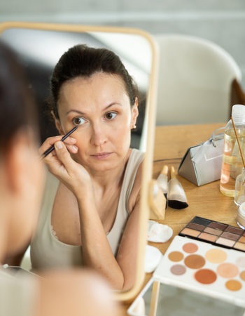 Woman drawing eyeliner wing in front of home vanity mirrorの写真素材