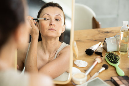 Woman applying eyeshadow with brush during daily makeupの写真素材