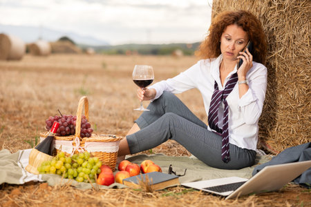 Woman in blouse and gray business suit is sitting next to haystack with mobile phoneの写真素材