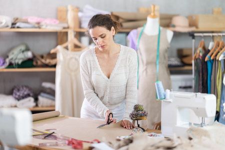 Female tailor cutting paper with scissors, cutting out the outline of pattern for a dress