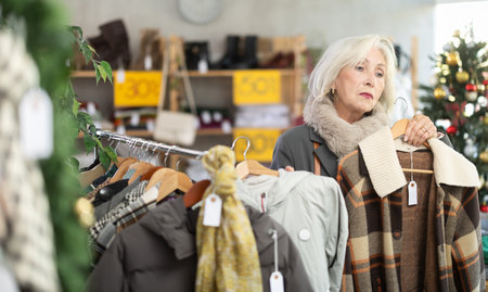 Attentive mature woman choosing coat or jacket in clothing storeの写真素材