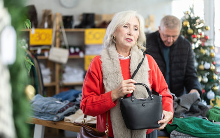 Mature woman standing and choosing handbag on Christmas tree backgroundの写真素材