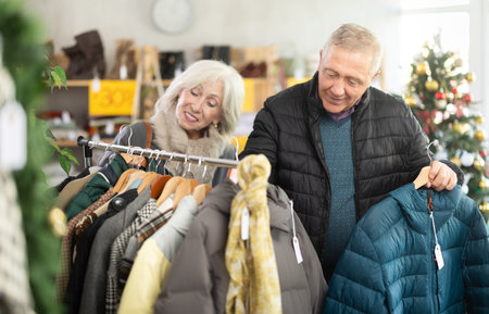Elderly married couple choose coat or jacket together in fashionable clothing storeの写真素材