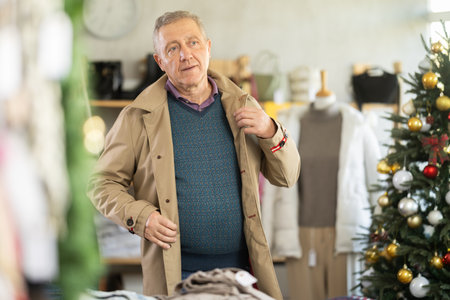 Mature man trying on coat trench coat in Christmas shopの写真素材