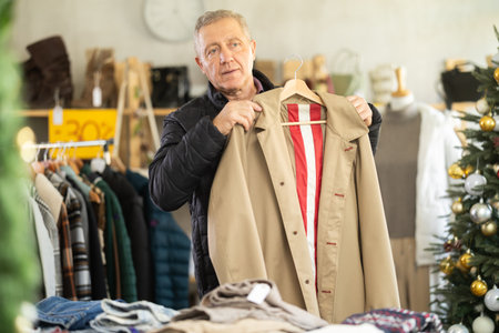 Elderly man chooses raincoat in clothing storeの写真素材