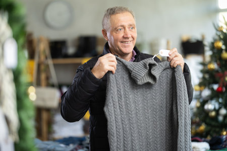 Mature male shopper selects sweater in fashionable clothing boutiqueの写真素材