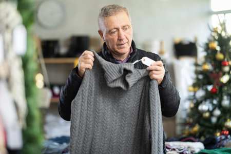 Mature male shopper selects sweater in fashionable clothing boutiqueの写真素材