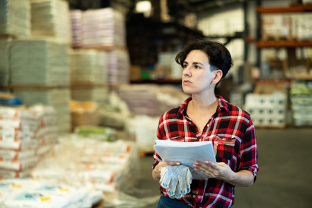 Female storekeeper checks availability of goods with documents in the building materials warehouseの写真素材