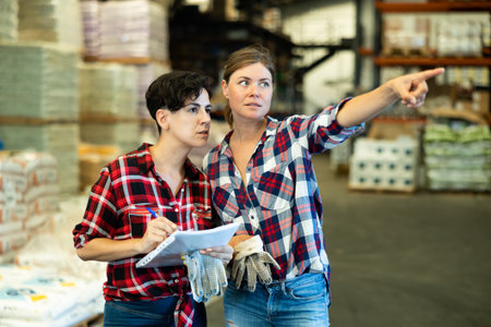 Manager talking with female worker in warehouse and pointing with his hand at boxes of productsの写真素材