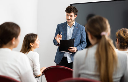 Positive skilled male coach explaining topic to group of people during foreign language class in...
