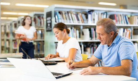 Man and woman in casual clothes searching in Internet and writing in planner in the book space libraryの写真素材