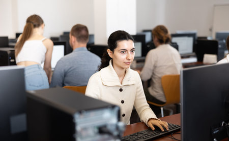 Girl student of computer courses looks at monitor screen, types on keyboard and does work
