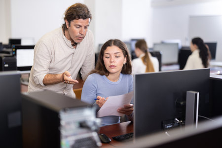Man teacher helps girl with learning on computer in university computer labの写真素材