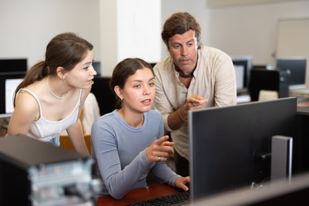 During computer lesson, two companions help girl student complete difficult taskの写真素材
