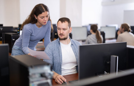 Female teacher helps man with learning on computer in university computer lab