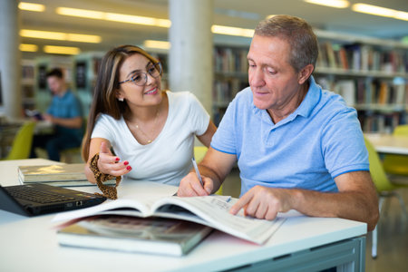 Young woman librarian helps an elderly man find the necessary information in laptopの写真素材