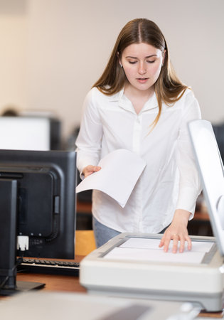 Girl puts paper document into copier, makes copy using office appliancesの写真素材